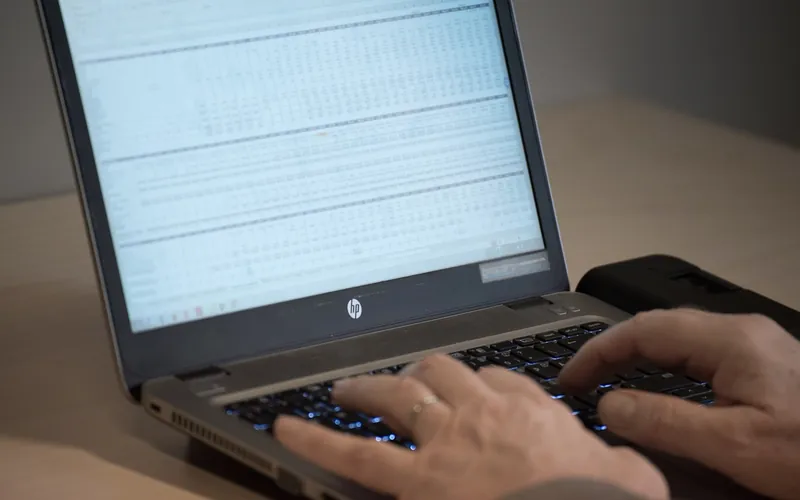 Gestionnaire de flotte VTC assis à son bureau dimanche soir, plusieurs feuilles Excel ouvertes sur l'écran, regardant des chiffres avec une expression concentrée
